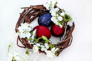 nido con Pasqua uova e rami di primavera fioritura ciliegie su un' bianca di legno sfondo. segale uova dipinto con naturale coloranti. foto