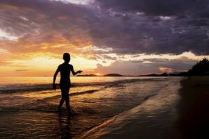 silhouette di ragazzo a piedi su il spiaggia a tramonto foto