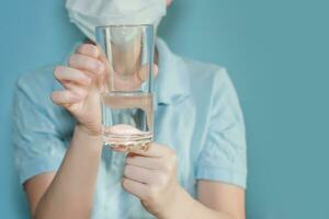 ragazzo nel protettivo medico maschera detiene bicchiere di acqua. conformità con il potabile regime. combattente coronavirus. bambino con influenza, influenza o freddo protetta a partire dal virus foto