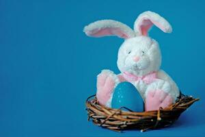 piccolo bianca giocattolo coniglietto nel nido con Pasqua blu uovo. Pasqua uova caccia concetto foto
