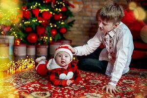 fratello con poco sorella a il nuovo anno albero. famiglia celebra Natale. 6 mesi vecchio poco ragazzo impara per strisciare foto