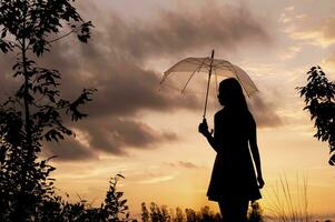 silhouette donna Tenere un ombrello a il tramonto tempo foto