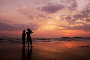 Due persone in piedi su il spiaggia a tramonto foto