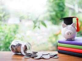 porcellino banca con la laurea cappello su colorato rilegato libri, bicchiere bottiglia e pila di monete. il concetto di Salvataggio i soldi per formazione scolastica, alunno prestito, borsa di studio, lezioni tasse nel futuro foto