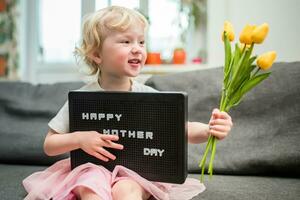 poco ragazza detiene un' mazzo di giallo tulipani e un' cartello quello dice contento La madre di giorno. bambino dà fiori per madre per vacanza. foto