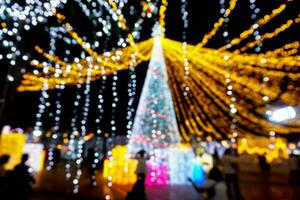 avvicinamento sfocato e bokeh di Natale vacanza illuminazione con persone a città tempo piazza su notte tempo sfondo. foto