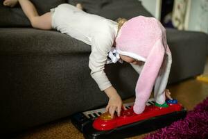 bambino giocando su sintetizzatore. un' poco ragazza bugie su un' grigio divano e giochi con un' figli di pianoforte. presto musica formazione scolastica per poco bambini, bambini a scuola, apprendimento musica strumenti foto