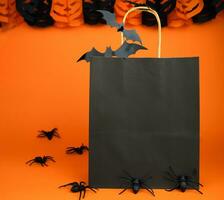 Halloween shopping e vendita concetto. carta nero Borsa e arredamento per Halloween su arancia sfondo. finto su. copia spazio. selettivo messa a fuoco. foto