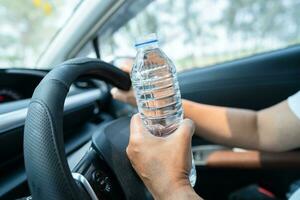 autista donna asiatica che tiene una bottiglia per bere acqua durante la guida di un'auto. la borsa dell'acqua calda in plastica provoca un incendio. foto