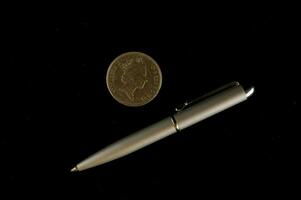 un' argento penna e un' moneta su un' nero sfondo foto