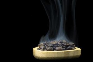il fumo sale dai chicchi di caffè nel piatto di legno foto