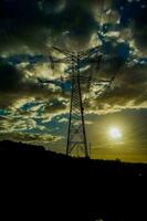 un' silhouette di un elettricità Torre contro un' nuvoloso cielo foto