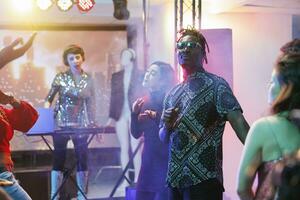 giovane persone danza e godendo discoteca festa nel discoteca. adulti fabbricazione energico si sposta per elettronico musica battiti su pista da ballo con faretti mentre avendo divertimento nel club foto