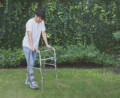 asiatico giovane uomo indossare aircast stivale a piedi nel il giardino con ortopedico camminatore. foto