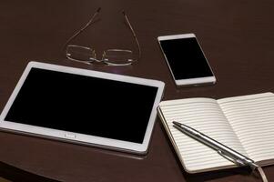 ufficio tavolo con mobile Telefono, tavoletta, occhiali, taccuino e penna con copia spazio. gadget su un' di legno tavolo foto