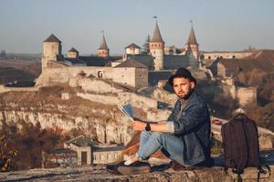 l'uomo viaggiatore con una mappa in mano si siede sullo sfondo del vecchio castello foto