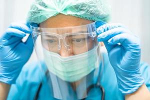 medico asiatico che indossa visiera e tuta in dpi protegge il coronavirus foto