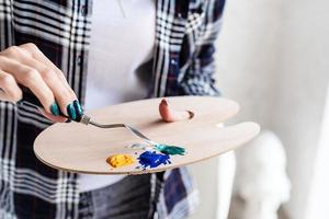 primo piano delle mani dell'artista donna che mescolano i colori sulla tavolozza d'arte in legno