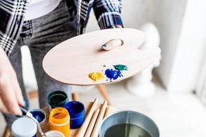primo piano delle mani dell'artista donna che mescolano i colori sulla tavolozza d'arte in legno