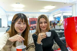 multietnico femmina amici siamo potabile caffè e guardare a il inteligente Telefono foto