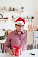 uomo con cappello da Babbo Natale saluta i suoi amici in video chat o chiama su tablet foto