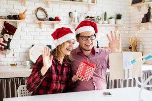 coppia in cappelli di Babbo Natale che saluta i loro amici in una videochiamata su tablet foto