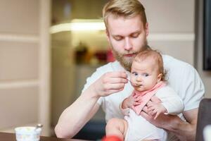 padre alimentazione il suo bambino con frutta puré a partire dal un' cucchiaio foto