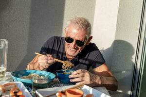 attraente di mezza età uomo avere divertimento mentre mangiare seduta a un' tavolo di cui Cinese prendere lontano cibo foto