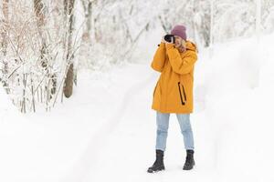 un' bellissimo ragazza con un' telecamera nel sua mani prende immagini di inverno nel un' nevoso parco foto