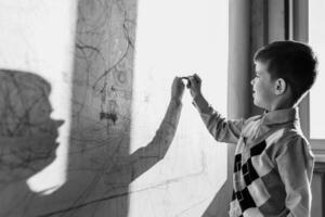 il bambino disegna su il parete con un' pastello. il ragazzo è impegnato nel creatività a casa. nero e bianca foto