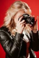 ritratto di un' bellissimo ragazza fotografo con un' telecamera nel sua mani chi è fotografato nel un' foto studio su un' rosso sfondo