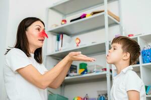 un' donna discorso terapista insegna un' bambino per soffio correttamente su colorato piume. foto
