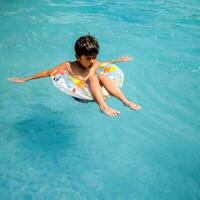 contento indiano ragazzo nuoto nel un' piscina, ragazzo indossare nuoto costume lungo con aria tubo durante caldo estate vacanze, bambini ragazzo nel grande nuoto piscina. foto
