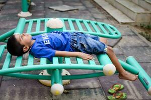 asiatico ragazzo fare routine esercizio nel società parco durante il mattina volta. carino poco ragazzo esercizio e Palestra per mantenere lui stesso in forma per vita. bambino esercizio all'aperto sparare foto