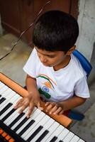 asiatico ragazzo giocando il sintetizzatore o pianoforte. carino poco ragazzo apprendimento Come per giocare pianoforte. del bambino mani su il tastiera interno. foto