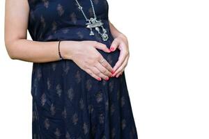 un' incinta indiano signora pose per gravidanza sparare e mani su pancia con bianca sfondo, indiano incinta donna mette sua mano su sua stomaco nel maternità vestito con pianura sfondo, gravidanza sparare foto