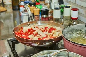 pezzi di pollo Seno con pomodori siamo fritte nel frittura padella su gas stufa foto