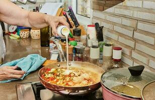 il capocuoco versa crema in pezzi di pollo Seno con pomodori, fritte nel un' frittura padella su un' gas stufa foto