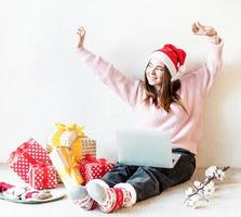 giovane donna con cappello da Babbo Natale che fa shopping online circondata da regali