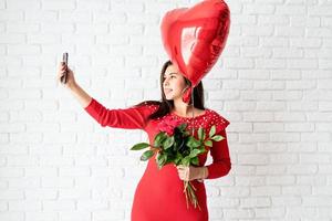 giovane donna in abito rosso con in mano un palloncino a cuore rosso e fiori foto