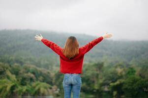 posteriore Visualizza Immagine di un' femmina viaggiatore seduta e Tenere prima colazione guardare a un' bellissimo montagna, fiume e natura Visualizza foto