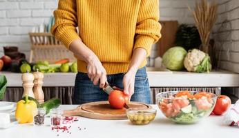 mani femminili che fanno insalata tagliando i pomodori in cucina foto