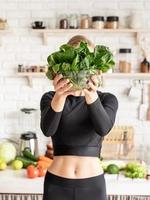 donna sorridente che tiene una ciotola di spinaci freschi in cucina foto