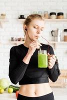 giovane donna che beve un sano frullato verde in cucina foto