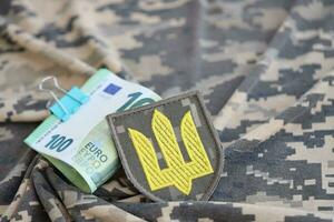 ucraino esercito simbolo e mazzo di Euro fatture su militare uniforme. pagamenti per soldati di il ucraino esercito a partire dal europeo unione, stipendi per il militare. guerra supporto foto