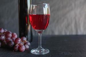 vino rosso e bottiglia di vino con uva su sfondo nero