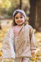 una bambina felice con un cappotto beige cammina nel parco autunnale foto