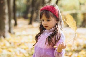 ritratto di una bambina felice che tiene una foglia nel parco autunnale foto