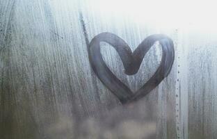 un' a forma di cuore disegno disegnato di un' dito su un' appannato bicchiere nel piovoso tempo metereologico foto