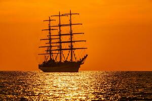 un' rosso ardente tramonto con il silhouette di andare in barca nave. marinai impostato vele su alberi di nave. bianca andare in barca nave galleggiante nel il mare. copia spazio. foto